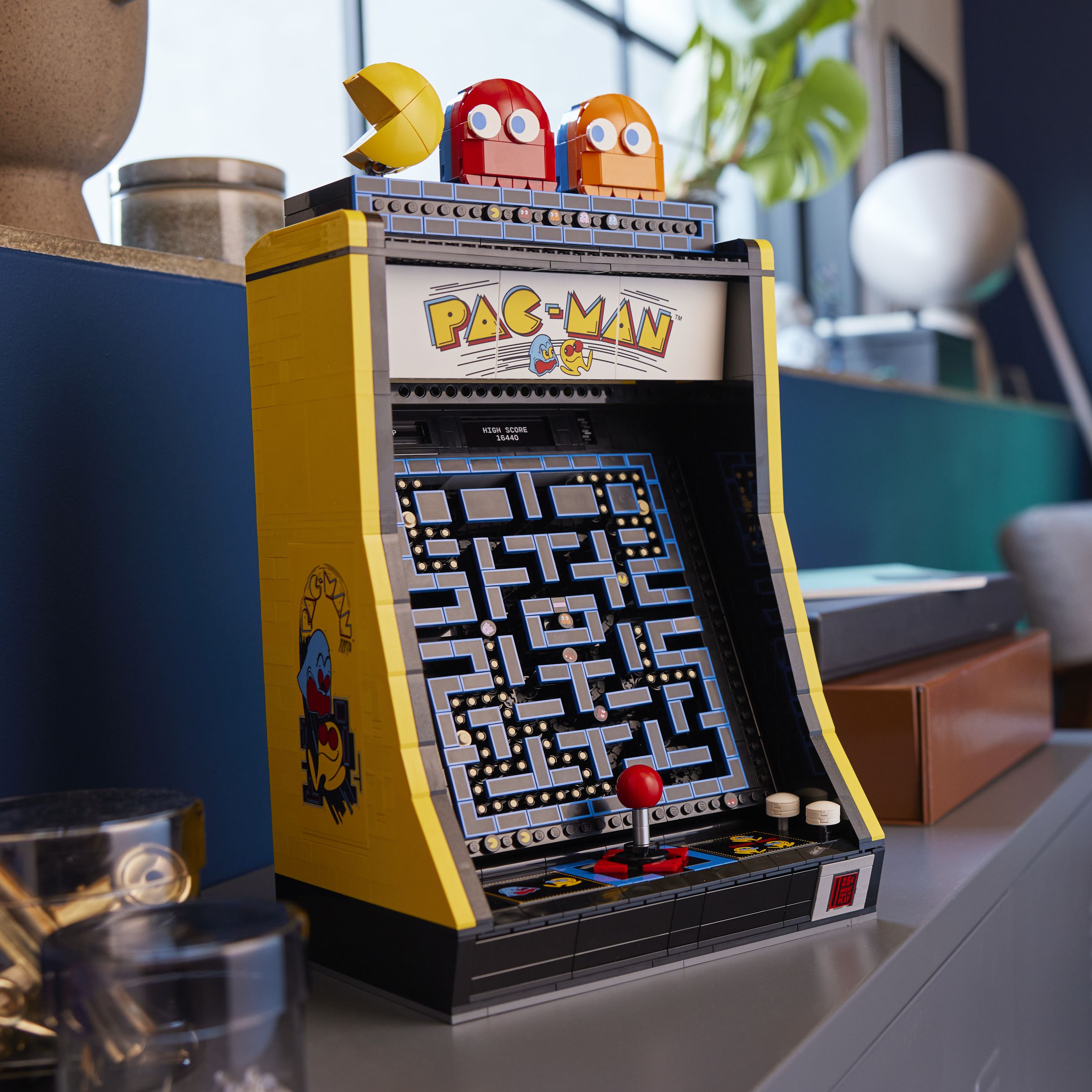 A lego pac-man arcade cabinet in a busy room.