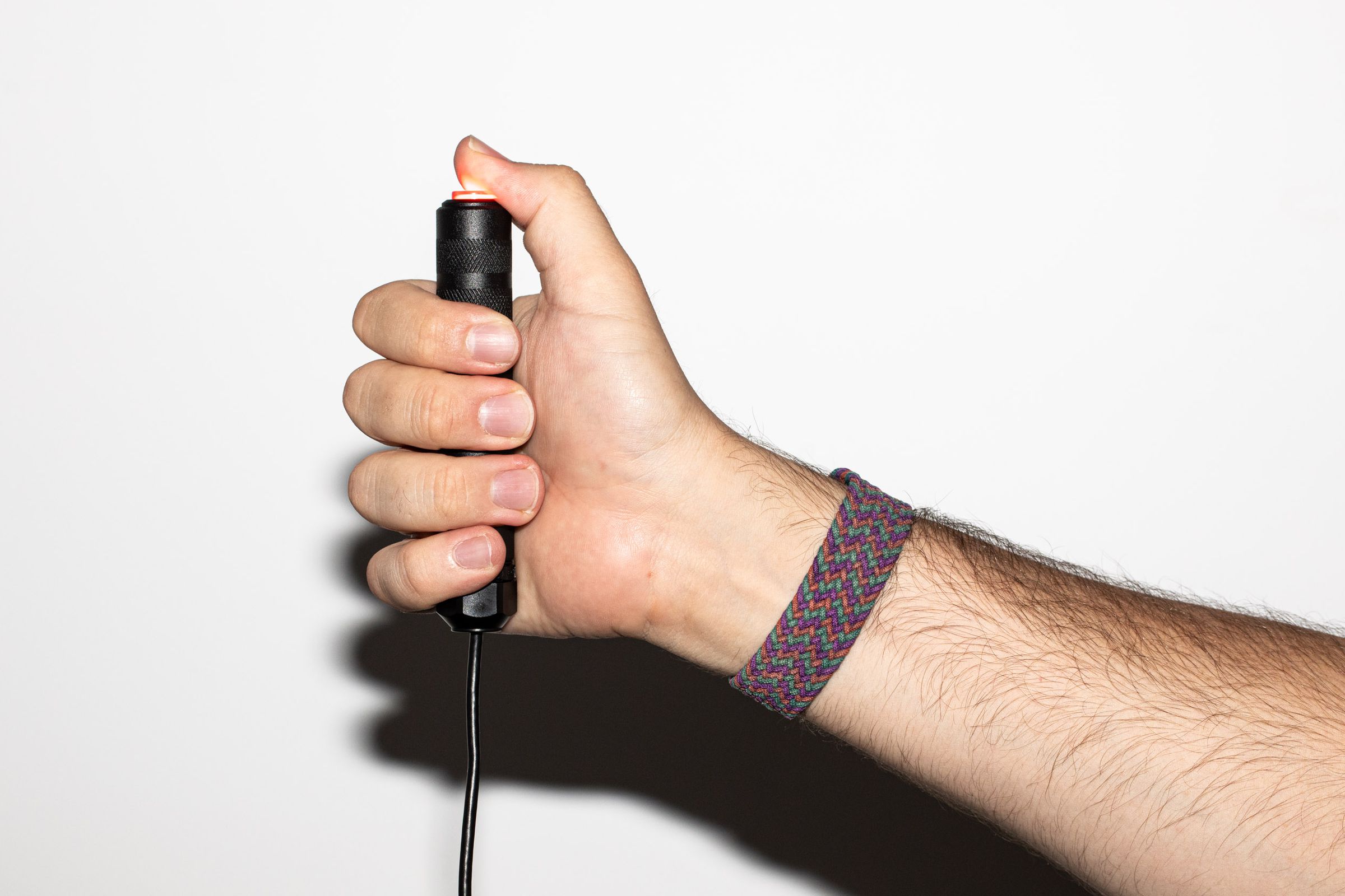 An arm grasps a fist-sized round black metal rod with a glowing red button on top, just underneath the thumb.