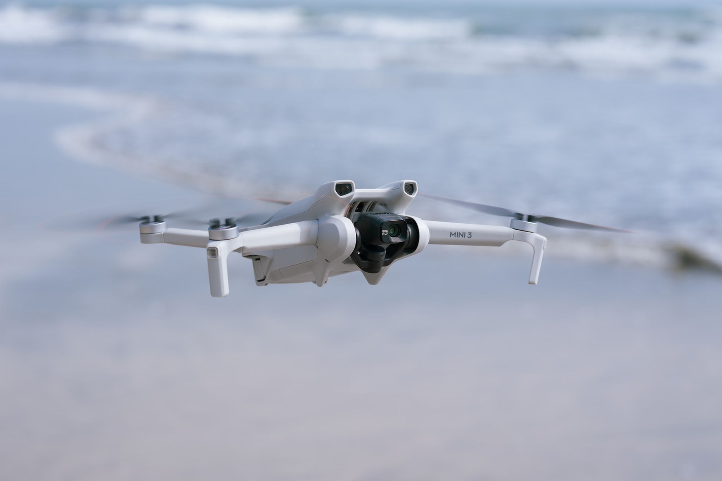 The DJI Mini 3 drone flying on the beach, with the sea in the background.