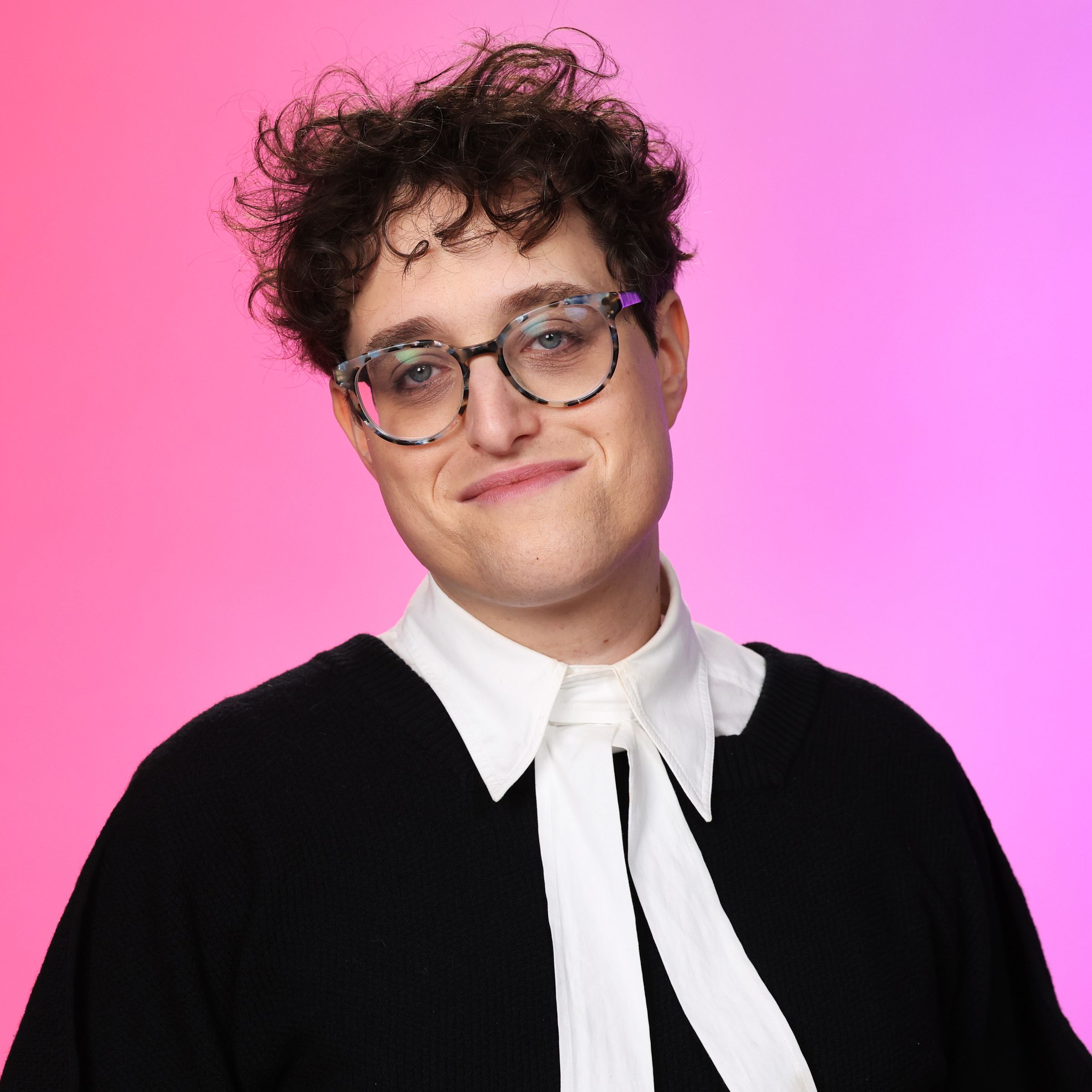 A close-up portrait shot of a nonbinary person wearing glasses, and a frock that resembles that of a court judge.