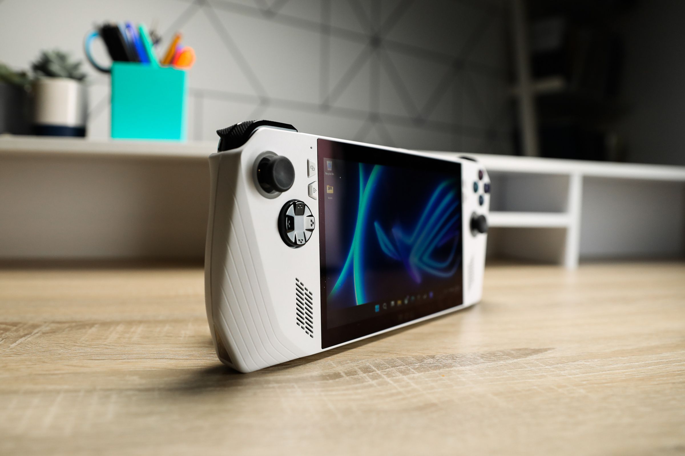 A white handheld with black joysticks and buttons sitting on a wooden desk with shallow depth of focus, at an angle to accentuate its profile.