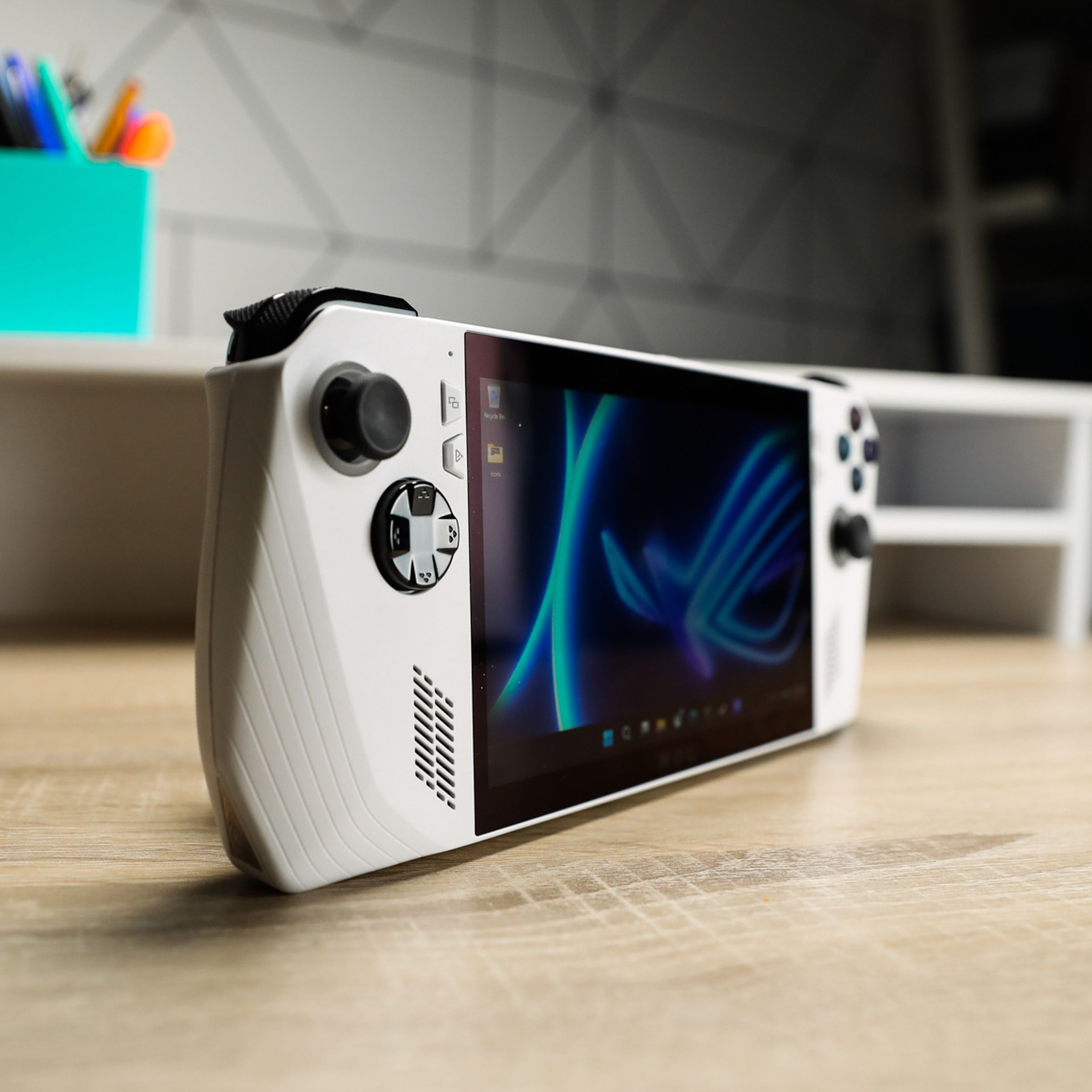 A white handheld with black joysticks and buttons sitting on a wooden desk with shallow depth of focus, at an angle to accentuate its profile.