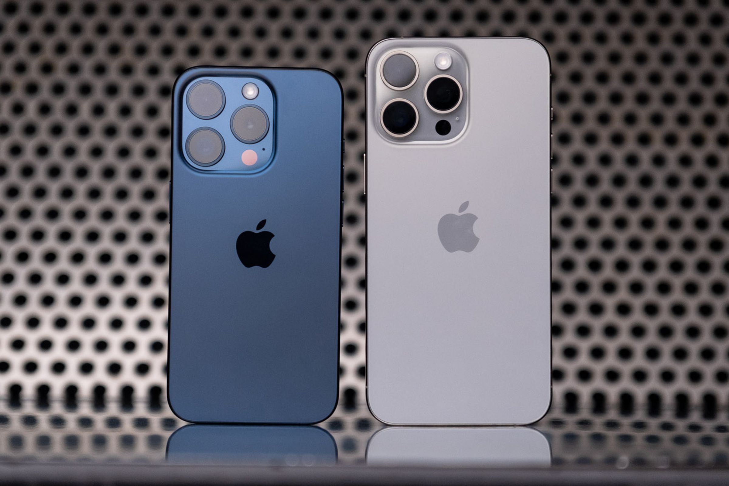The iPhone 15 Pro (blue titanium) and 15 Pro Max (white titanium) standing next to one another.