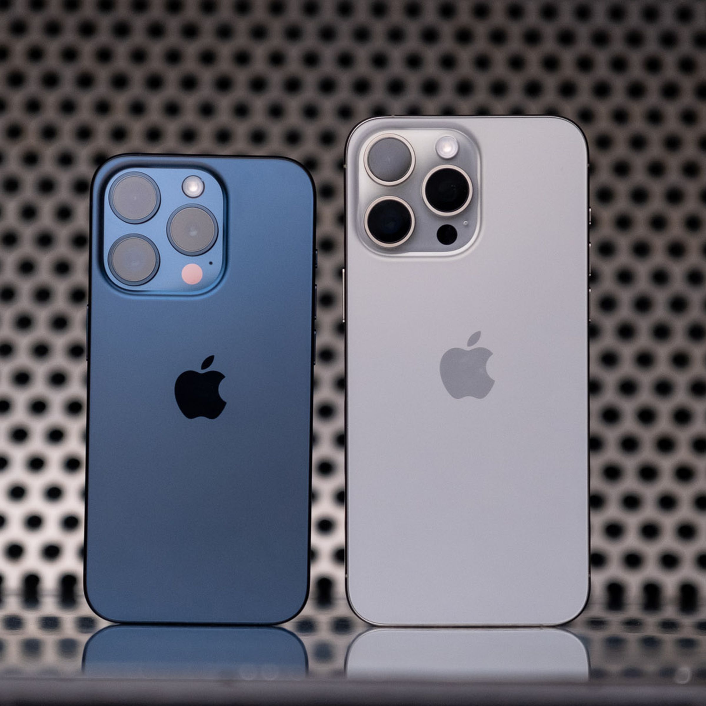 The iPhone 15 Pro (blue titanium) and 15 Pro Max (white titanium) standing next to one another.