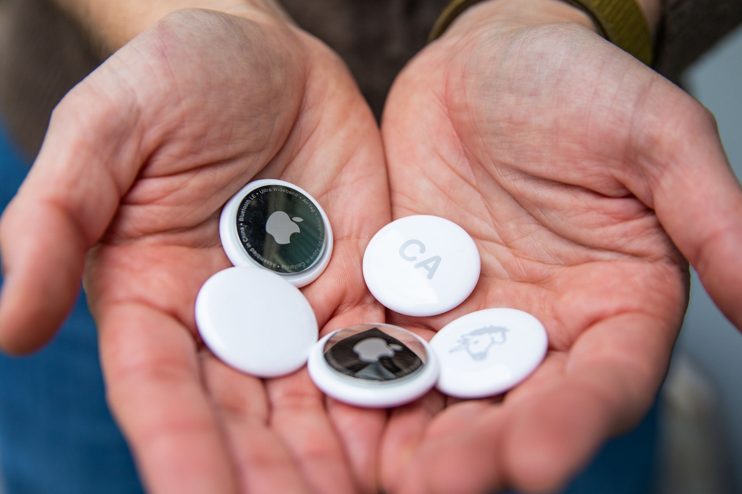 A close-up image depicting a set of hands holding a selection of Apple AirTags.