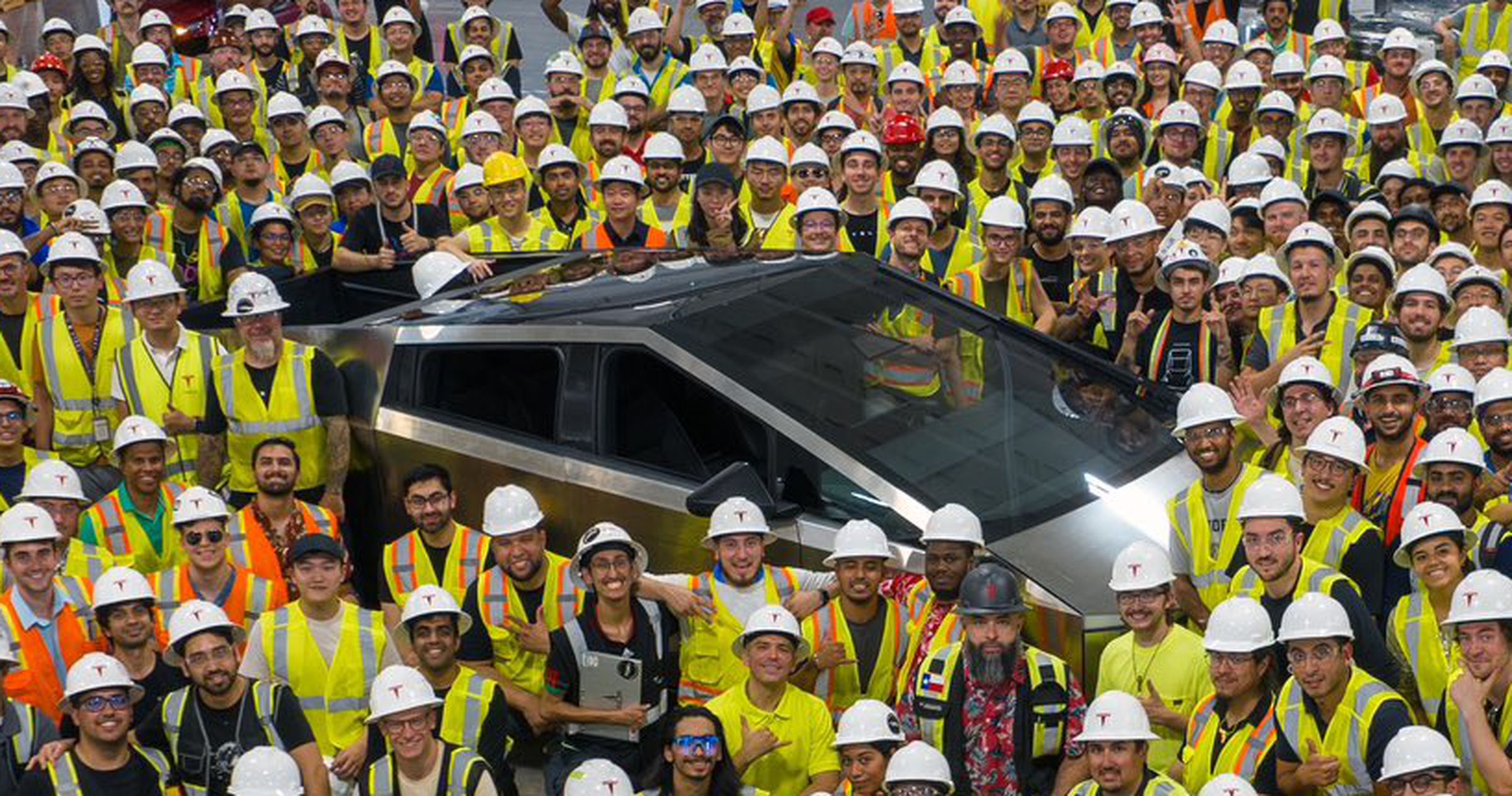 Tesla Cybertruck pickup shown surrounded by factory workers.