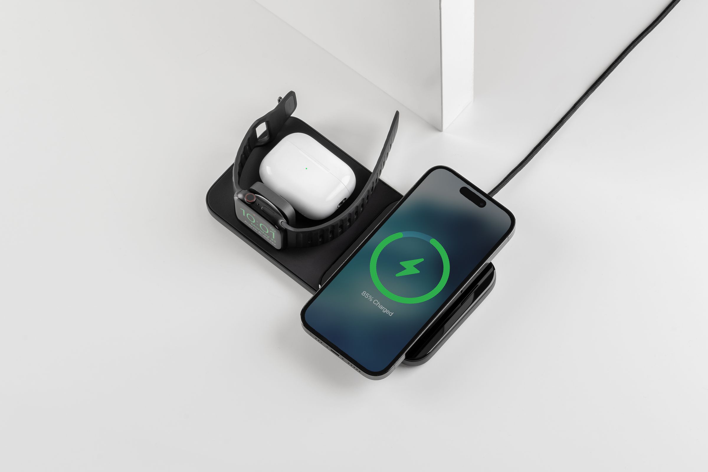 An iPhone, Apple Watch, and AirPods case charging on a black Nomad Base One Max 3-in-1 charger.