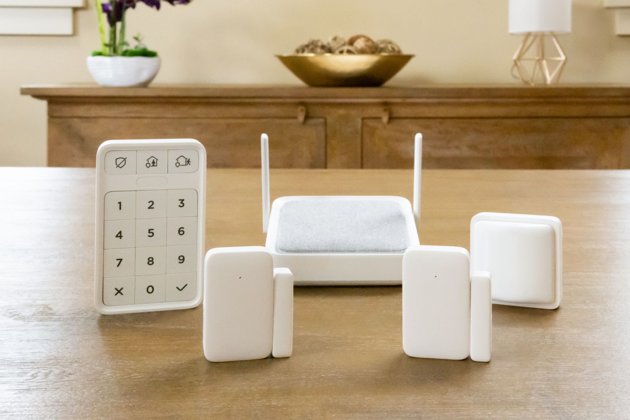 A five-piece white security system on a wooden tabletop in a living room.