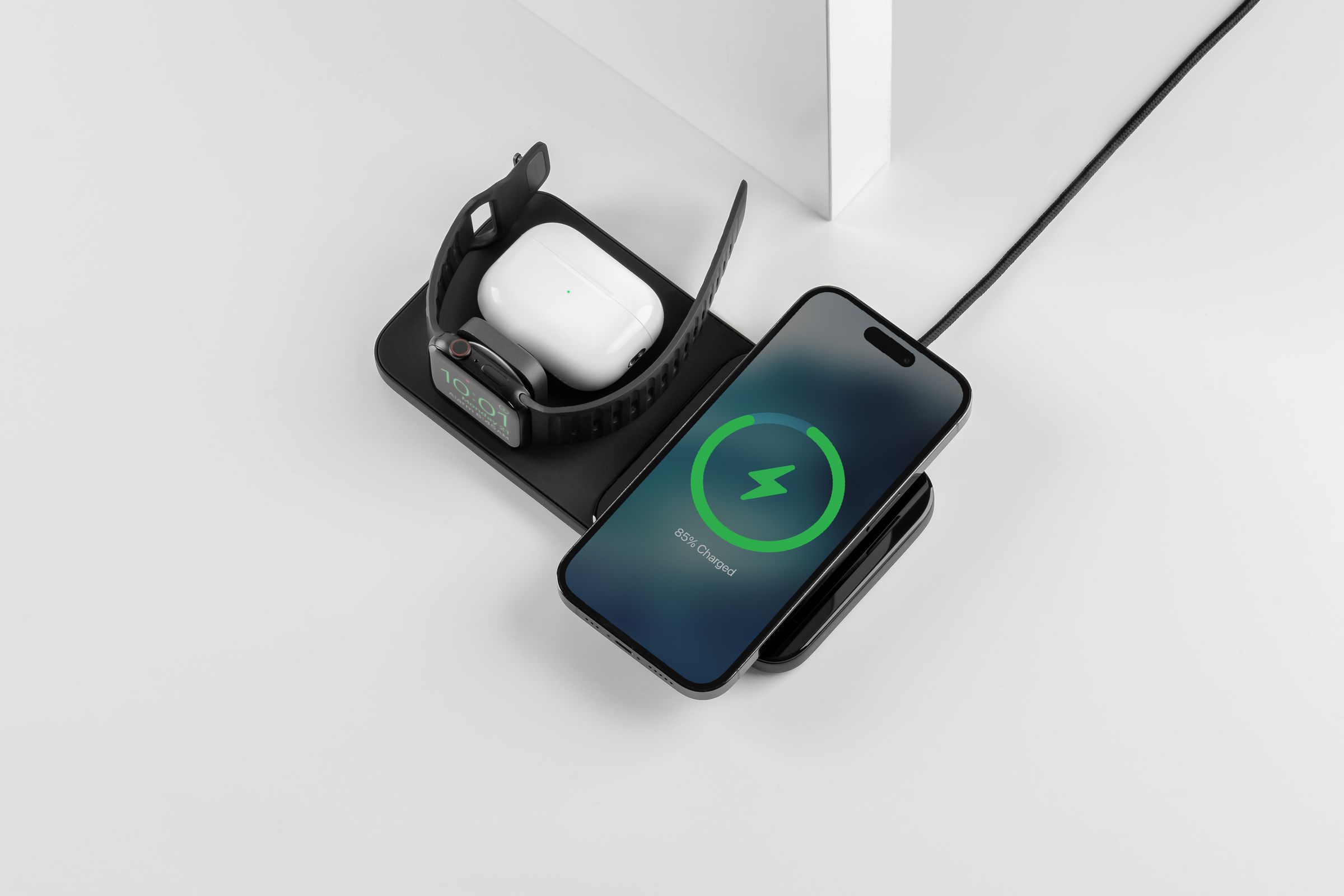 An iPhone, Apple Watch, and AirPods case charging on a black Nomad Base One Max 3-in-1 charger.