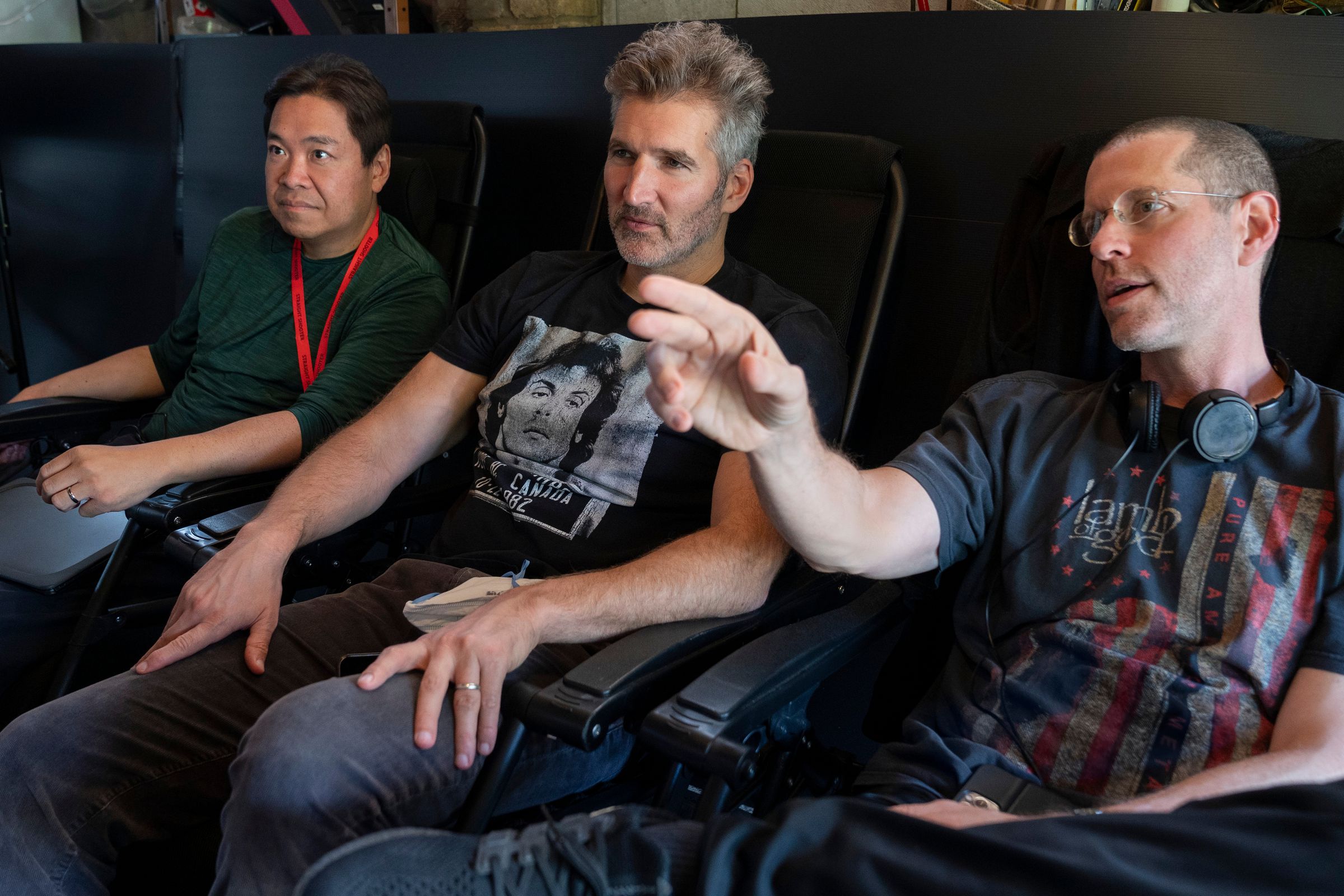 Three men wearing T-shirts and jeans while sitting in a trio of chairs.